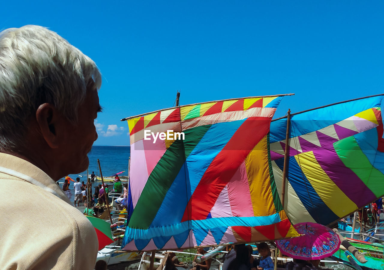 REAR VIEW OF MAN ON BEACH AGAINST BLUE SKY