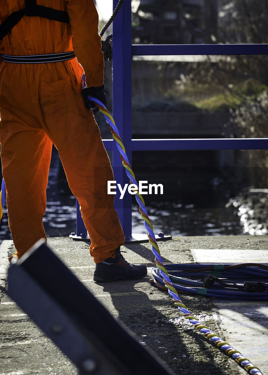 Low section of firefighter with rope standing on bridge