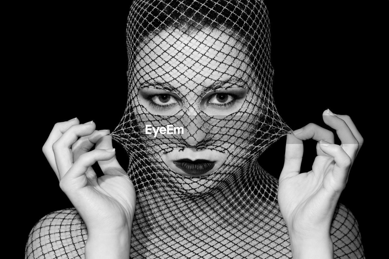 Close-up portrait of woman wearing lipstick and netting against black background