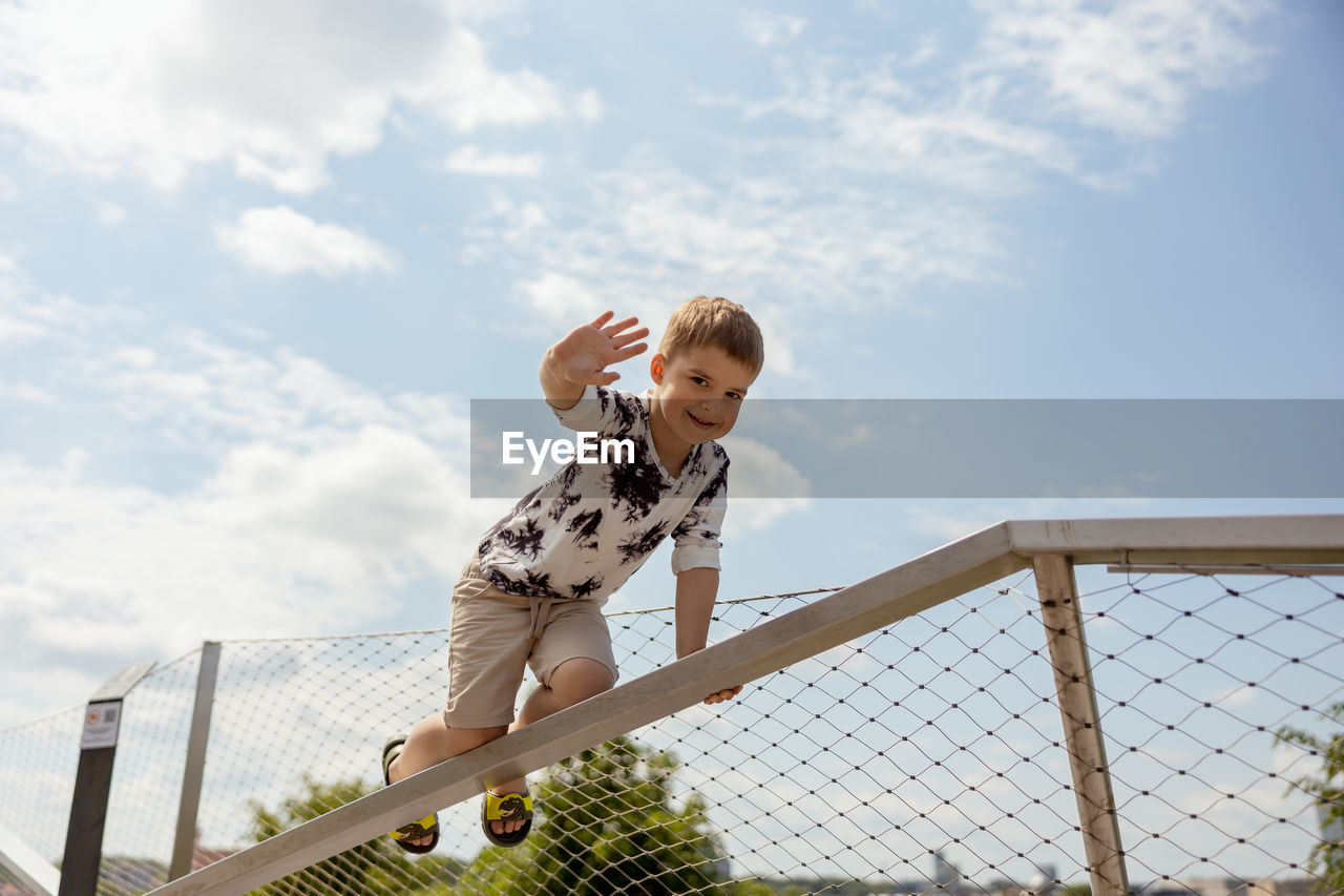 Adorable caucasian boy climbing on metal handrail outdoor. cute child having fun in the city