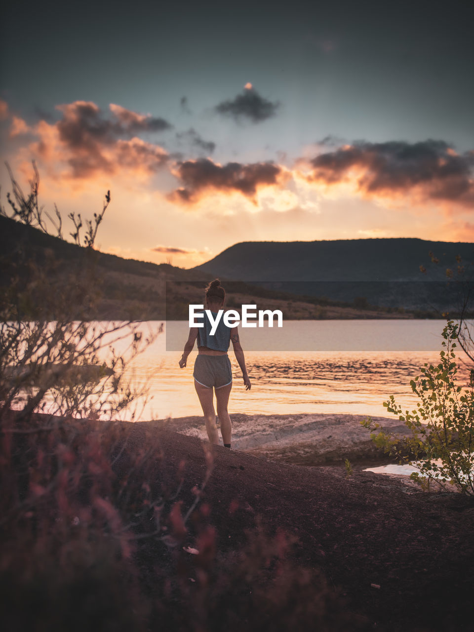 Rear view of man standing on beach against sky during sunset