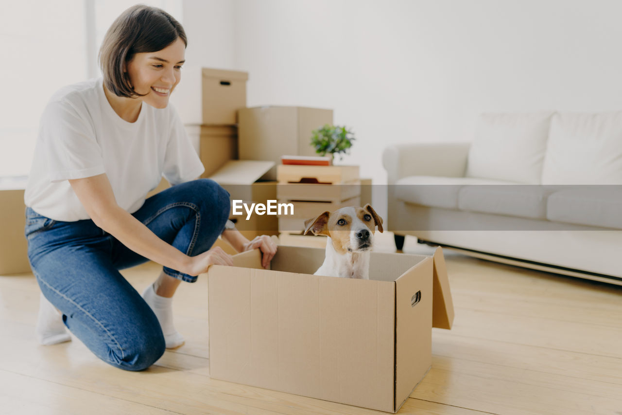 Woman with dog crouching by sofa at home