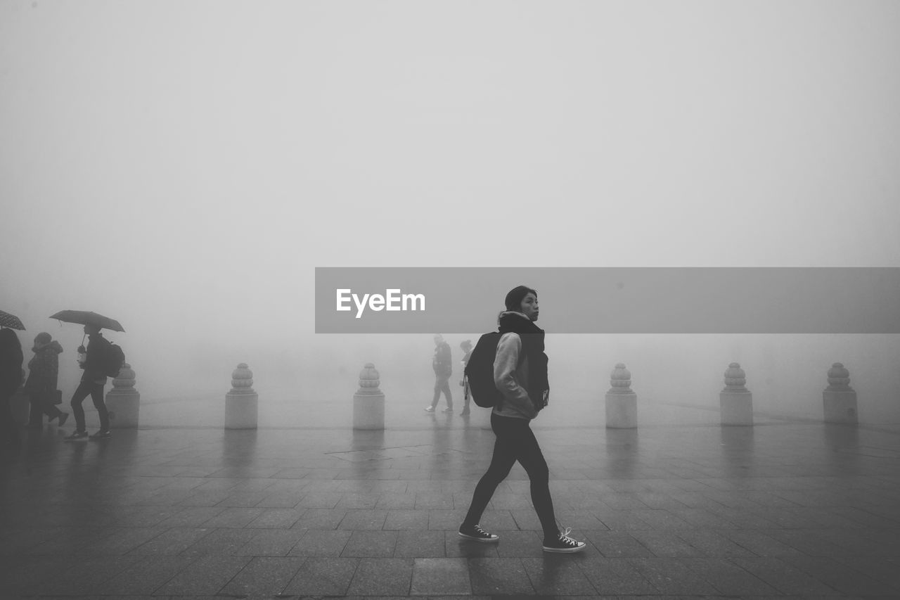 Full length on woman walking at pedestrian zone against sky during foggy weather