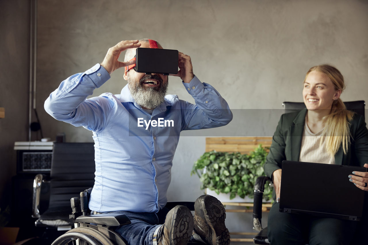 Blond businesswoman looking at businessman wearing vr simulator in creative office