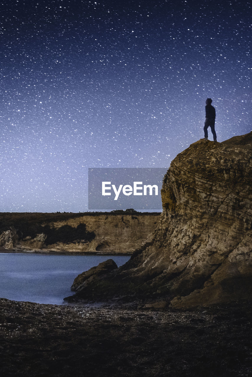 Silhouette man standing on cliff against sky at night