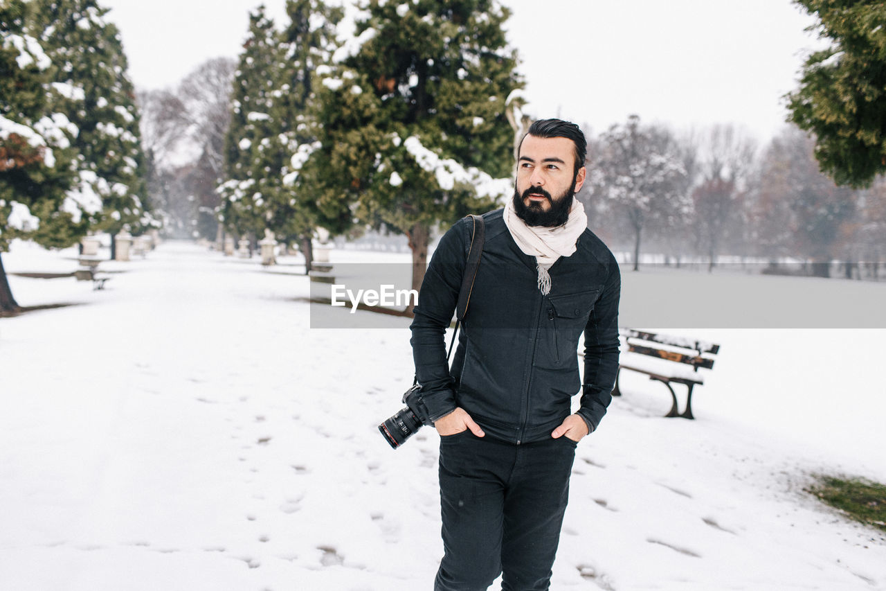 Handsome man with camera standing on snow covered footpath during winter