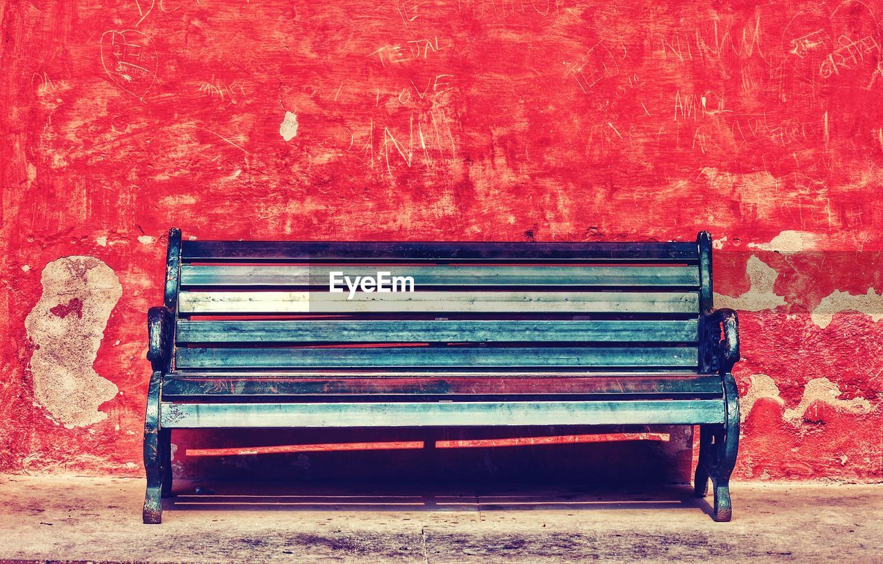 Empty bench against red weathered wall