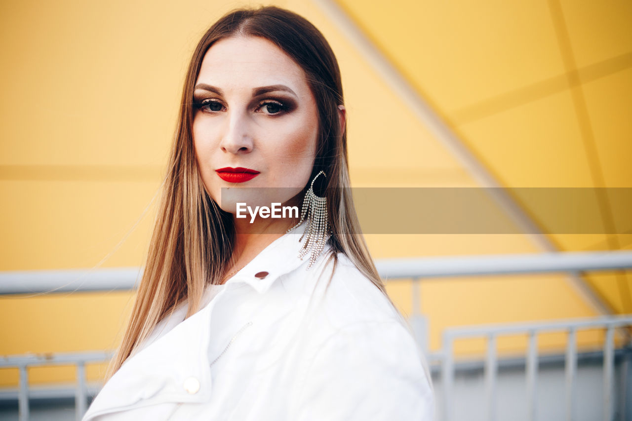 Portrait of beautiful woman wearing earring against yellow building