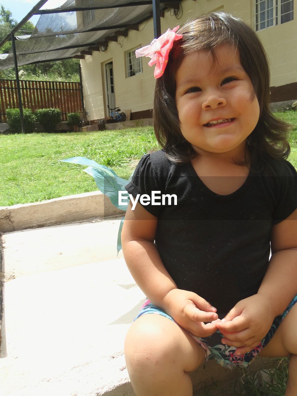 Close-up of girl looking away while sitting against house during sunny day