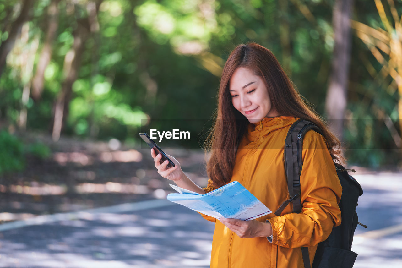 Smiling woman using mobile phone while holding map