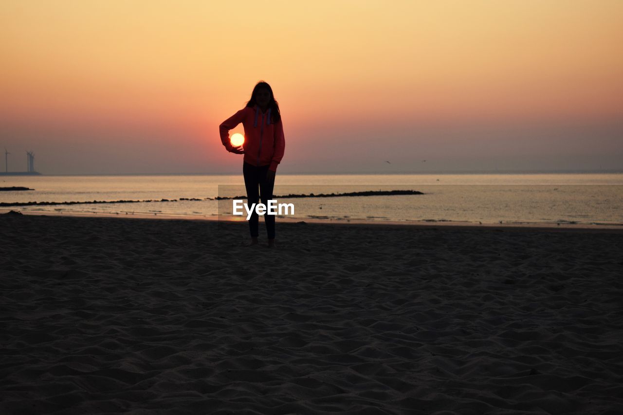 REAR VIEW OF WOMAN AT BEACH DURING SUNSET