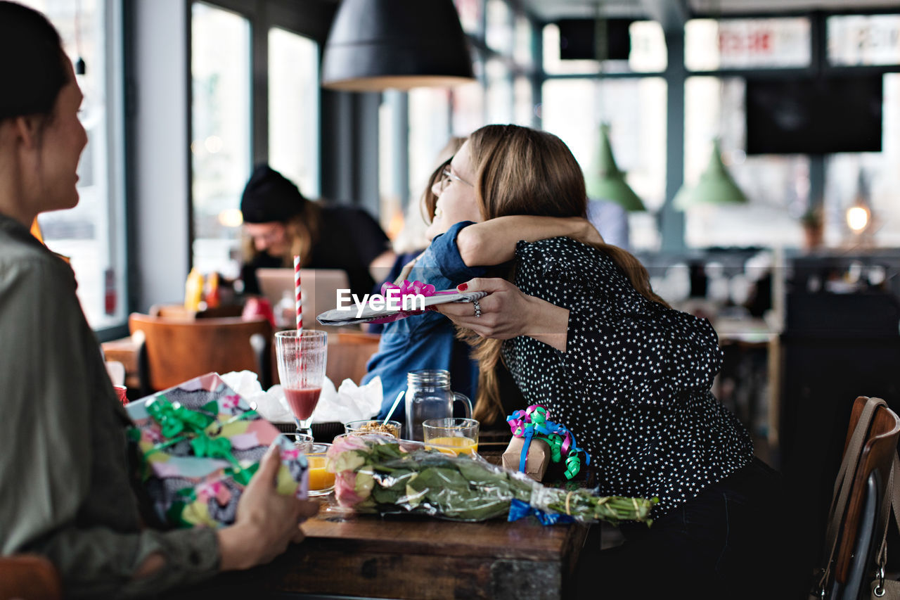 Young woman looking at female friends embracing while sitting at restaurant