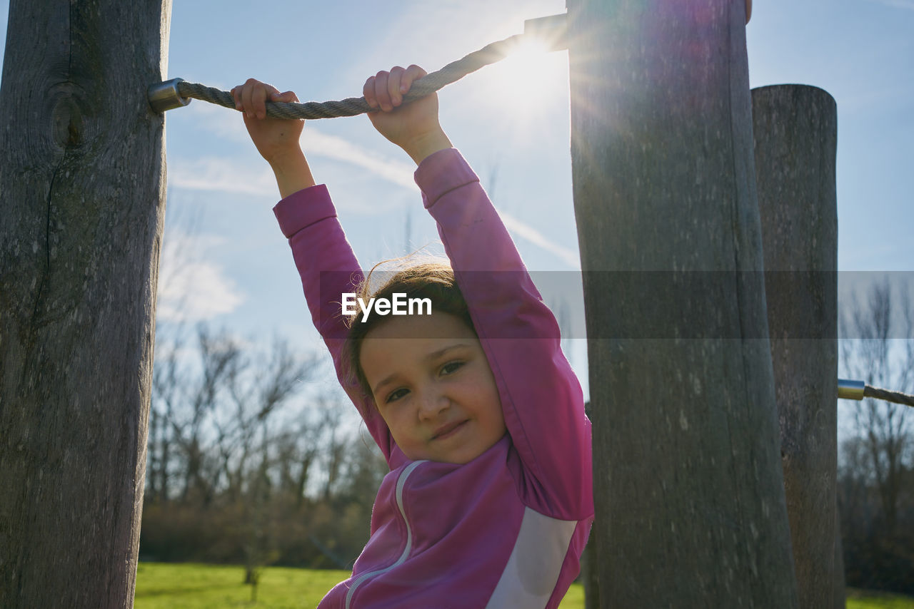 Girl on ropes and zip lines looks into camera with the sun in the background