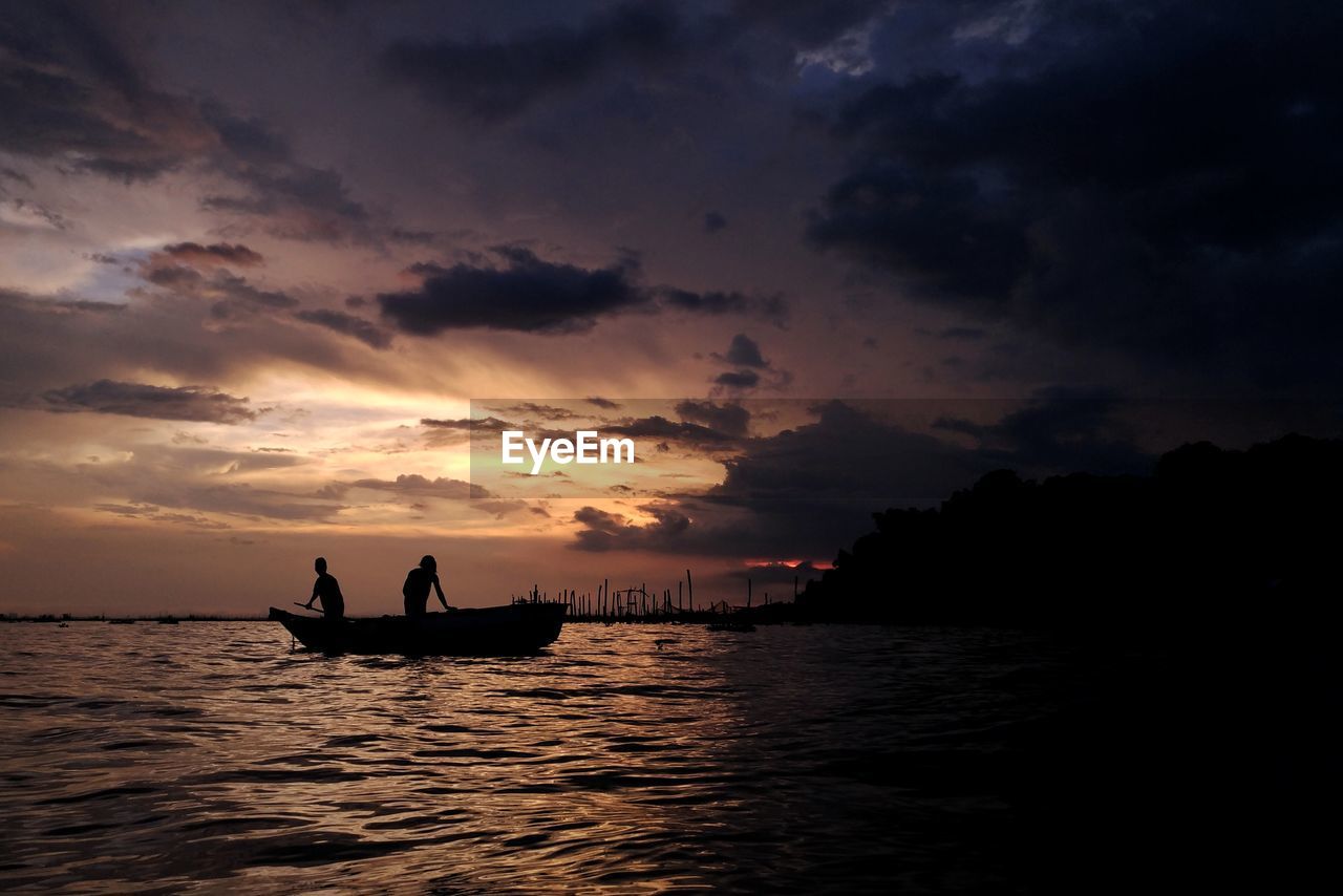 Silhouette people fishing on sea during sunset