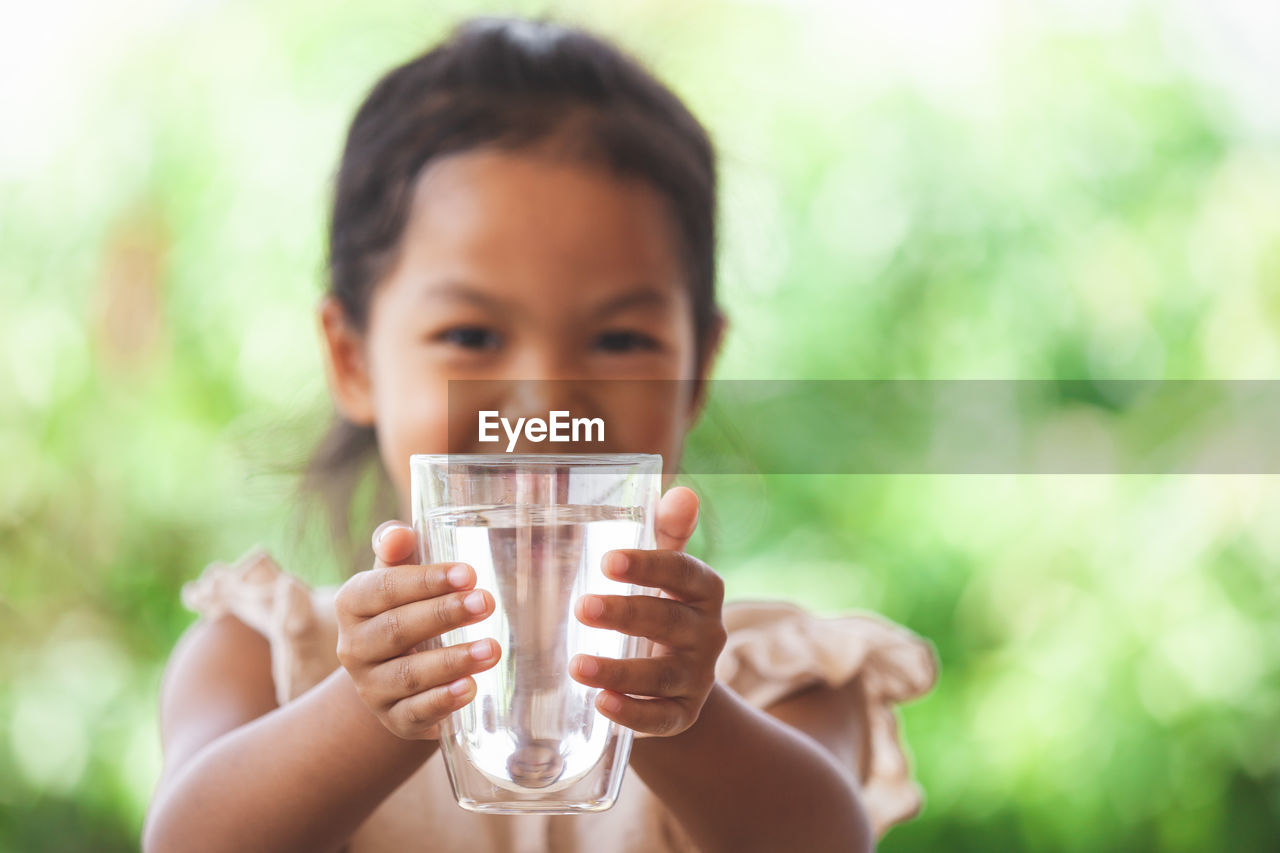 Close-up portrait of girl holding water glass outdoors