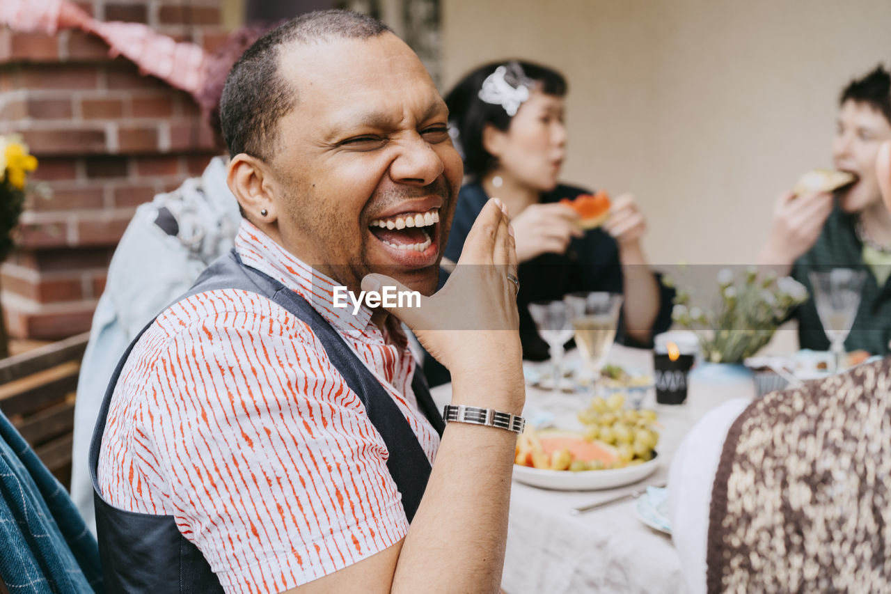 Cheerful gay man laughing while enjoying during party with friends in back yard