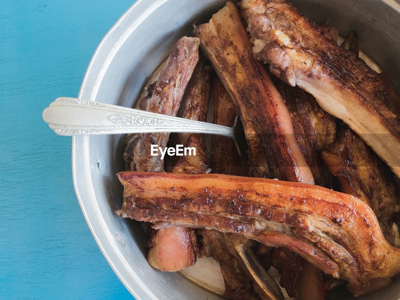 High angle view of pork with spoon in container against blue table