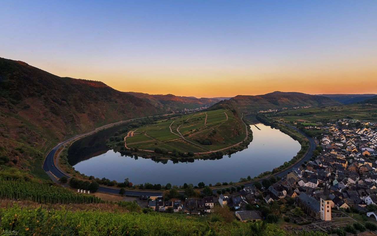 Scenic view of river and mountains against sky during sunset in town