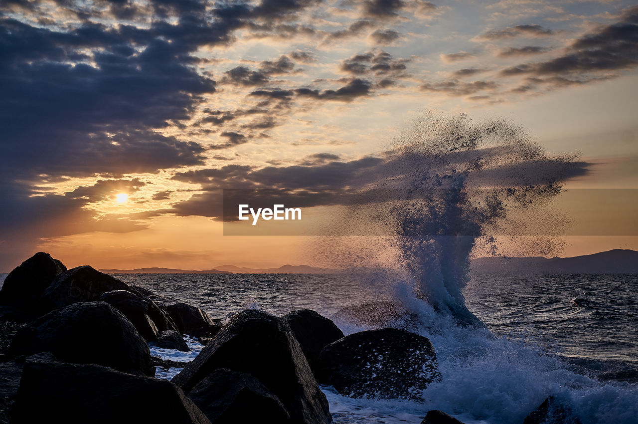 SEA WAVES SPLASHING ON ROCKS AT SHORE AGAINST SKY