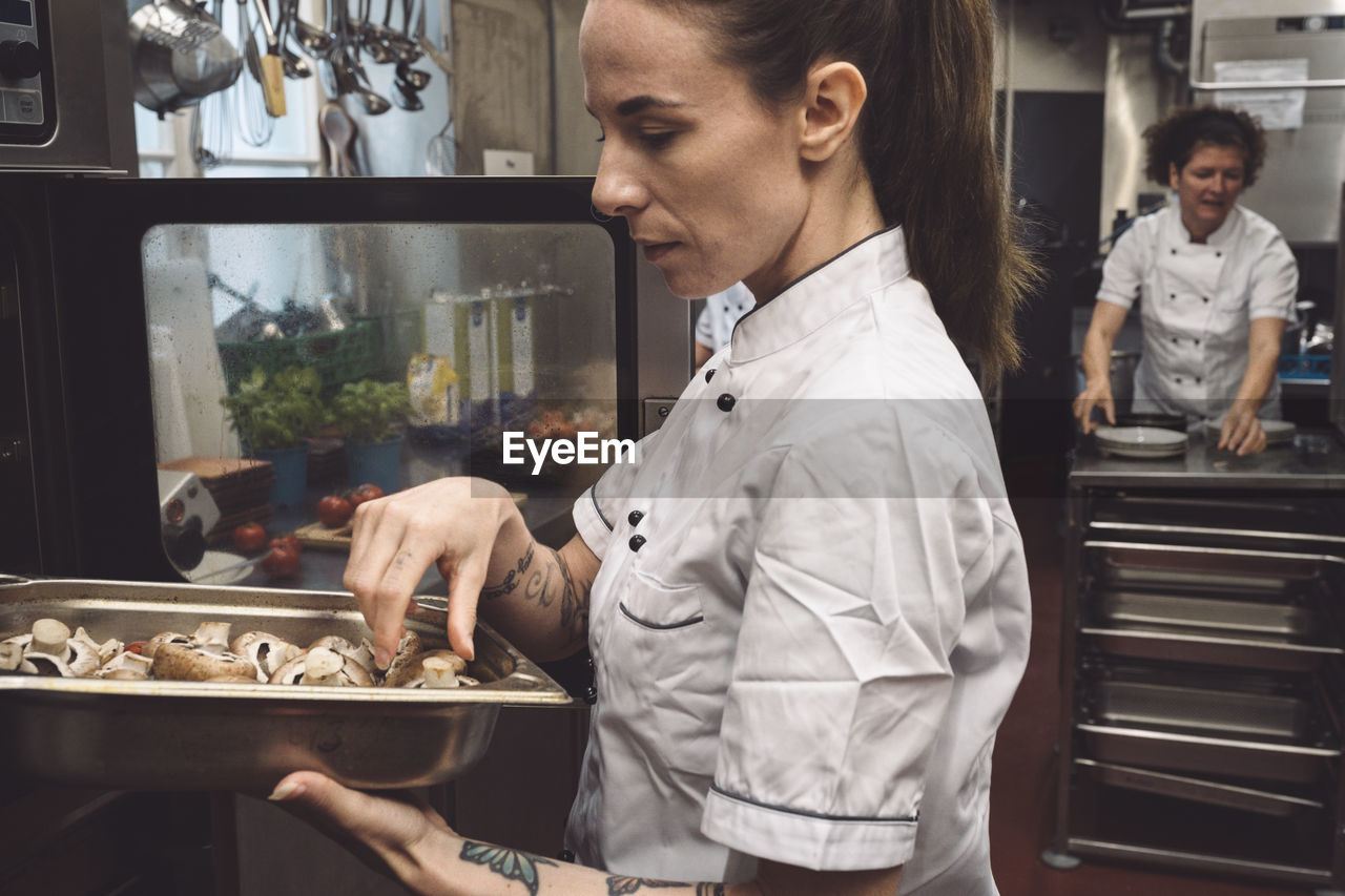 Side view of chef baking mushrooms in oven at commercial kitchen