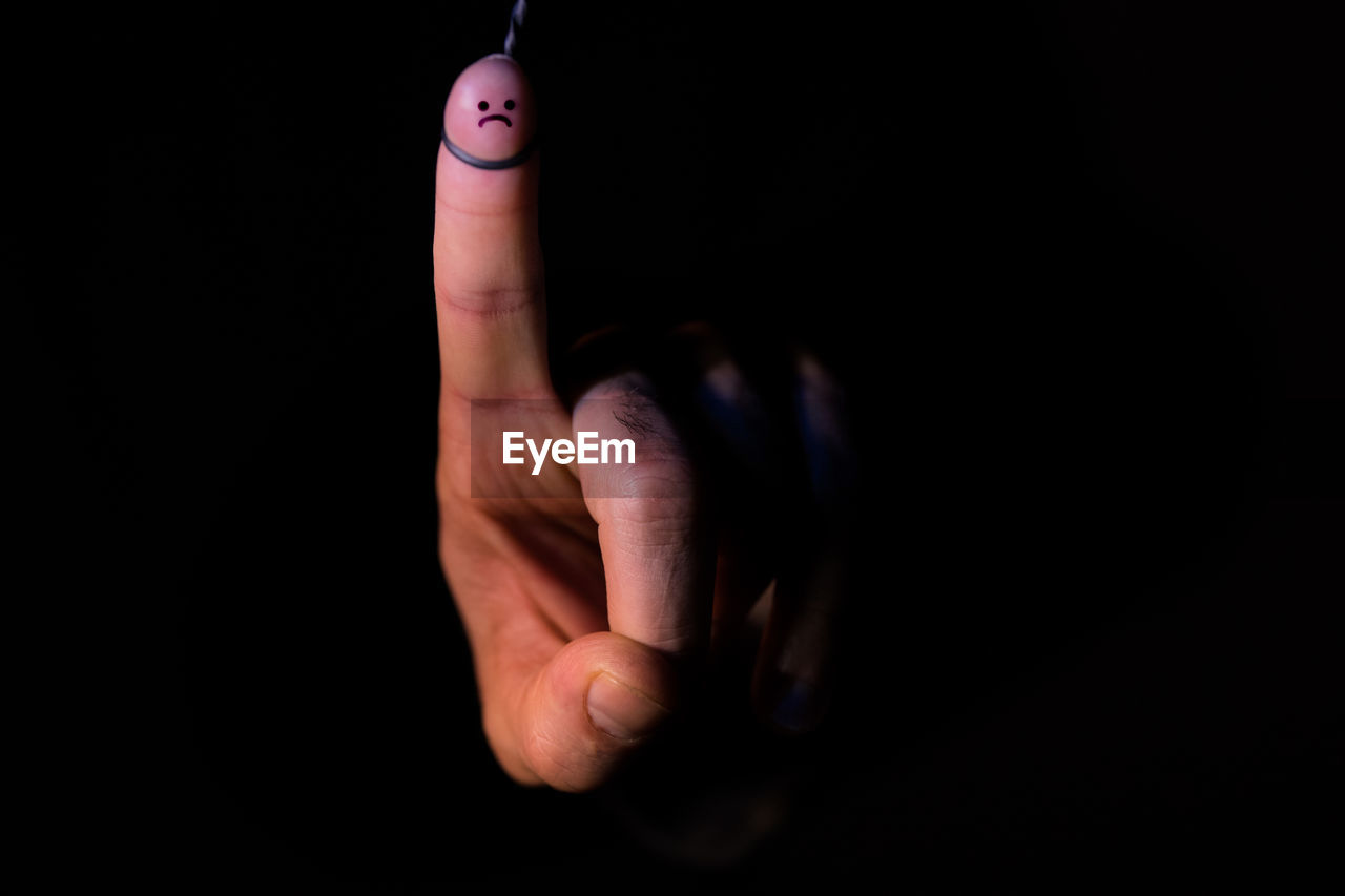 Close-up of human hand with anthropomorphic face against black background
