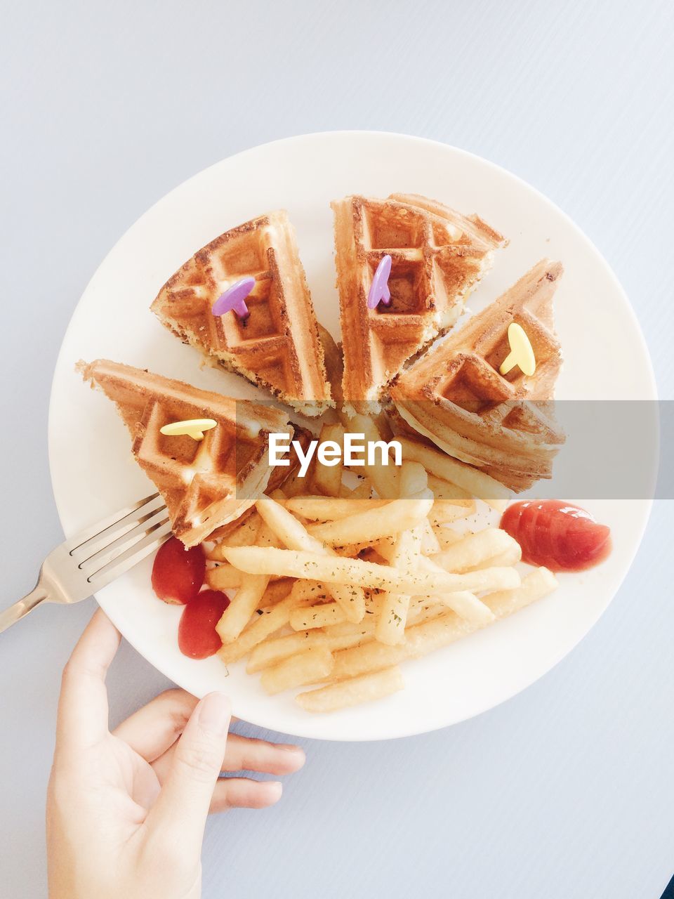 Cropped hand holding plate of french fries and waffles