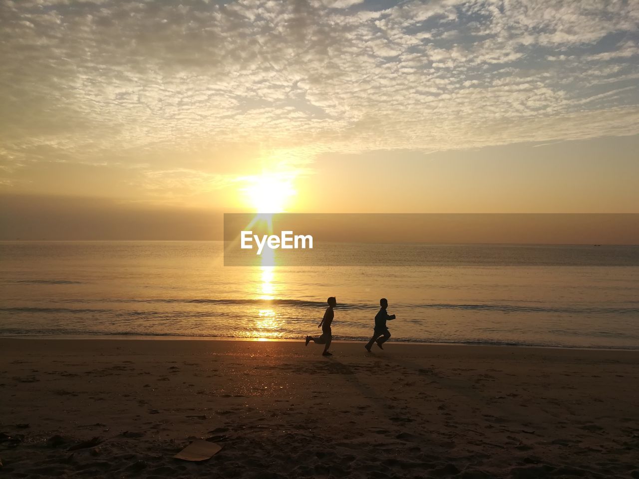 Silhouette boys running at beach against sky during sunset