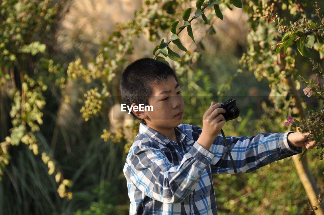 Teenage boy photographing plants at public park