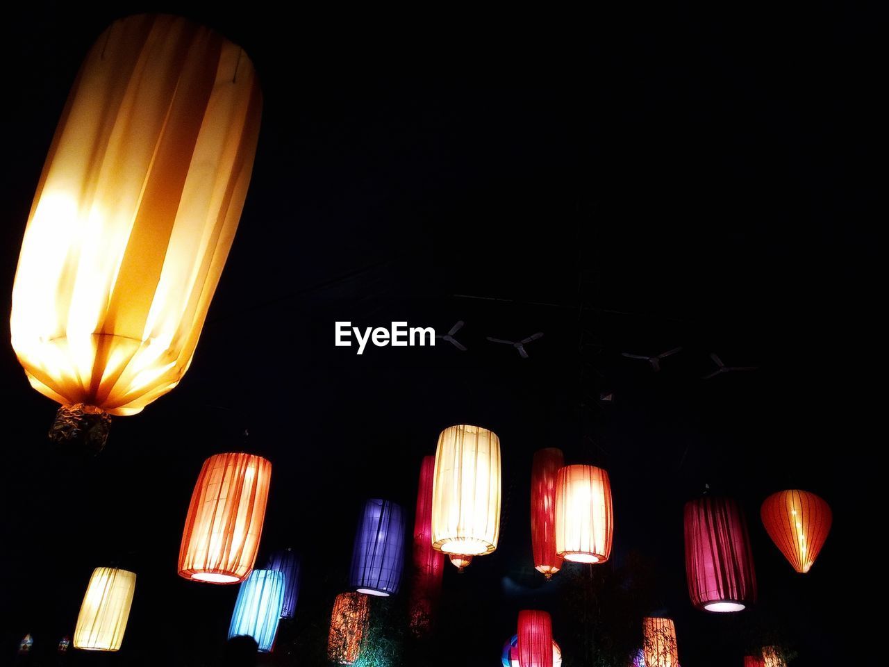 LOW ANGLE VIEW OF ILLUMINATED LANTERNS HANGING IN DARK