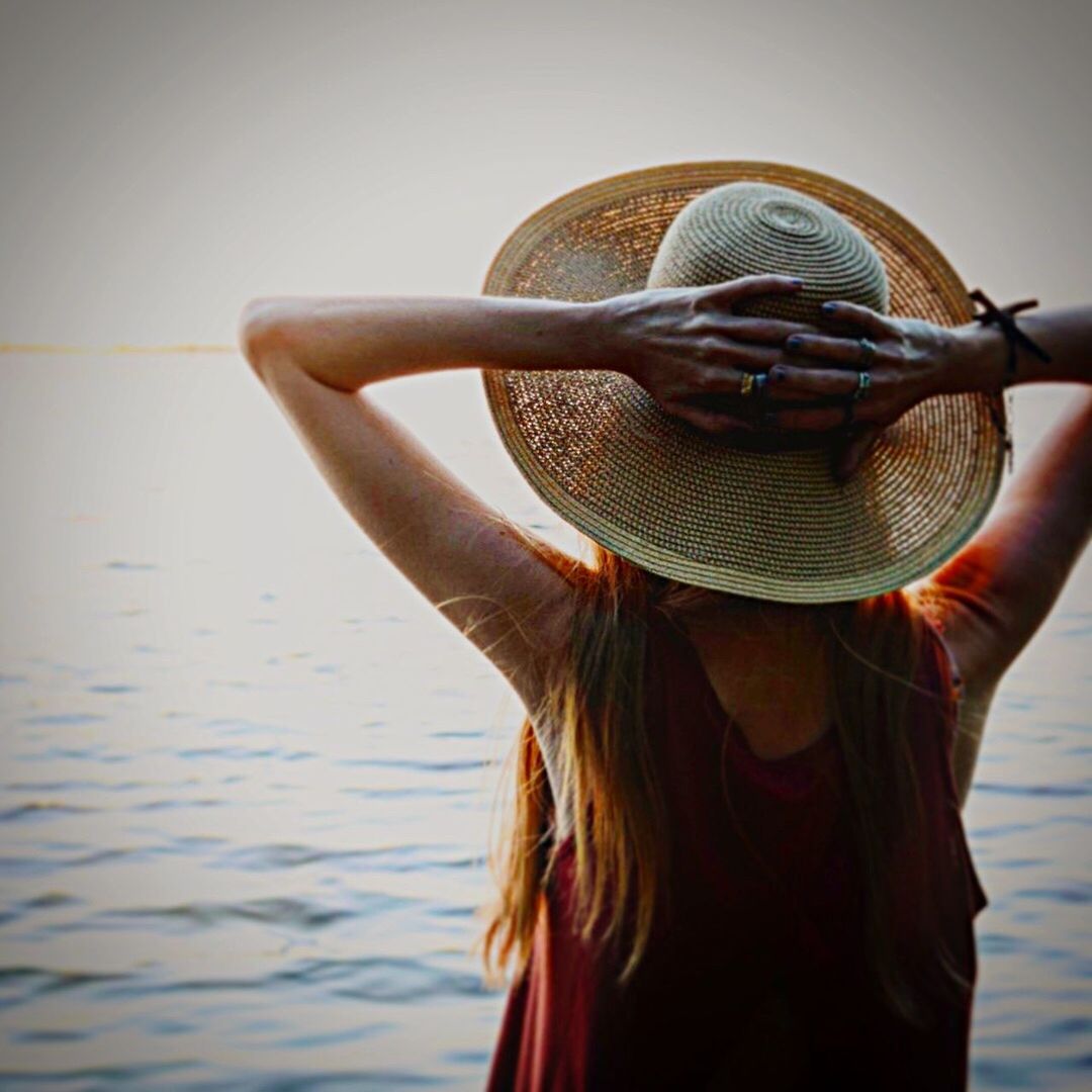 Rear view of woman with hat standing by lake