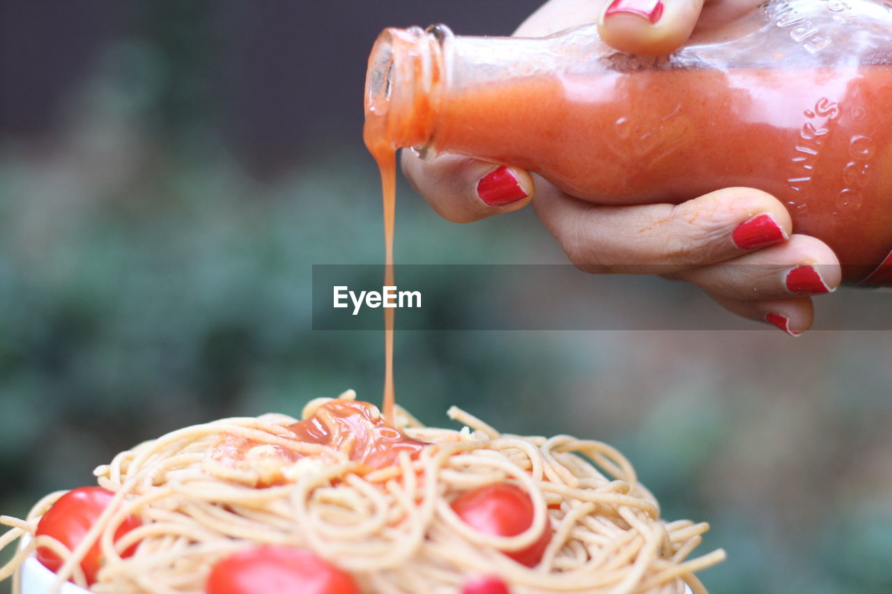 Cropped hand of woman pouring sauce on noodles