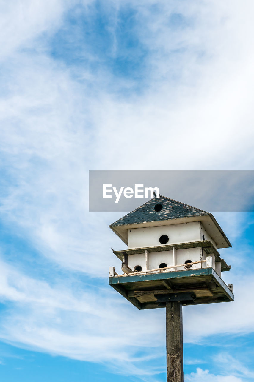 Low angle view of birdhouse on against sky - big 2 storey birdhouse with nests and a solo bird. 