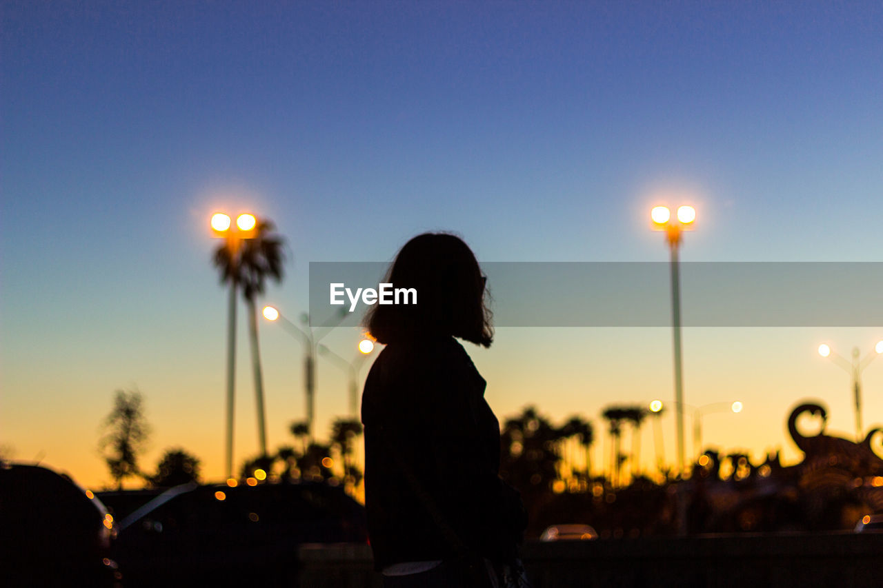 Silhouette woman standing on street against sky during sunset