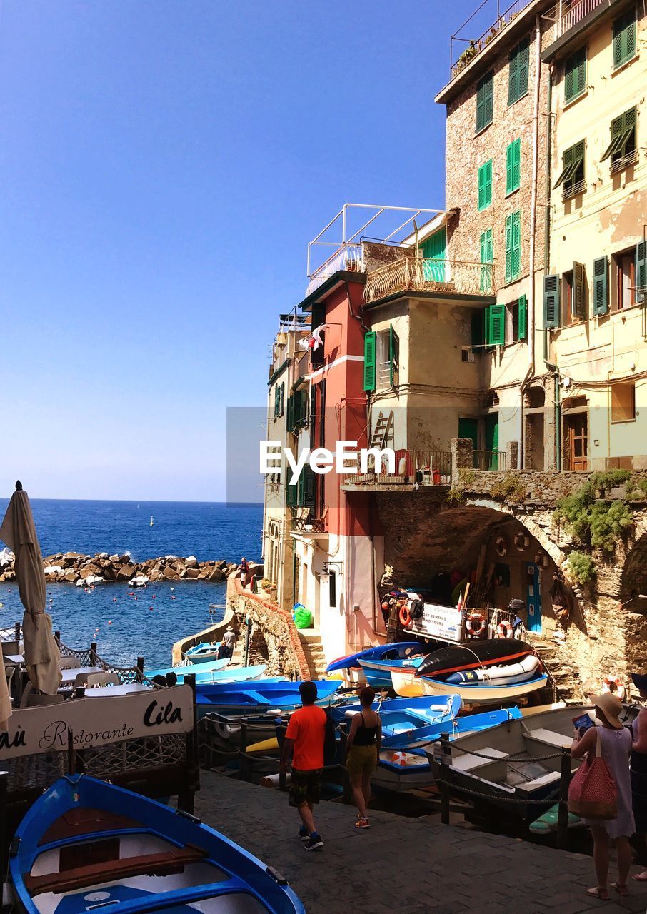 PEOPLE ON BEACH BY BUILDINGS AGAINST CLEAR SKY