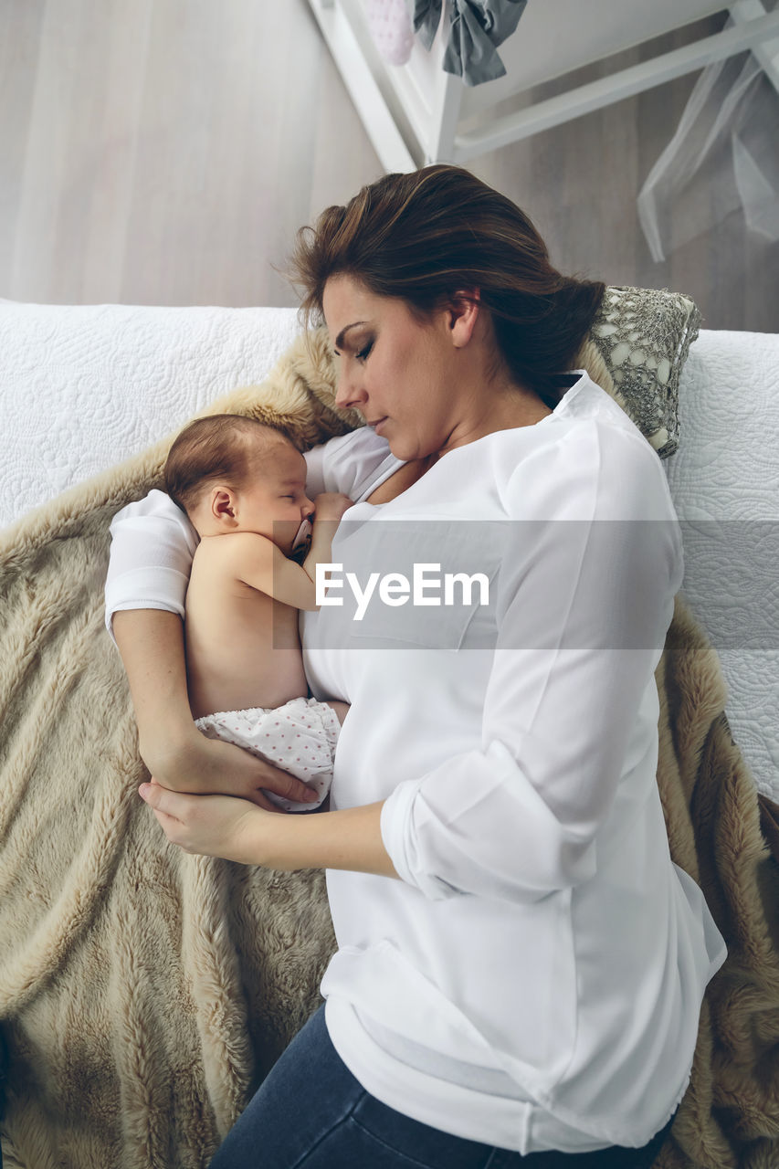 High angle view of mother breastfeeding daughter on bed at home