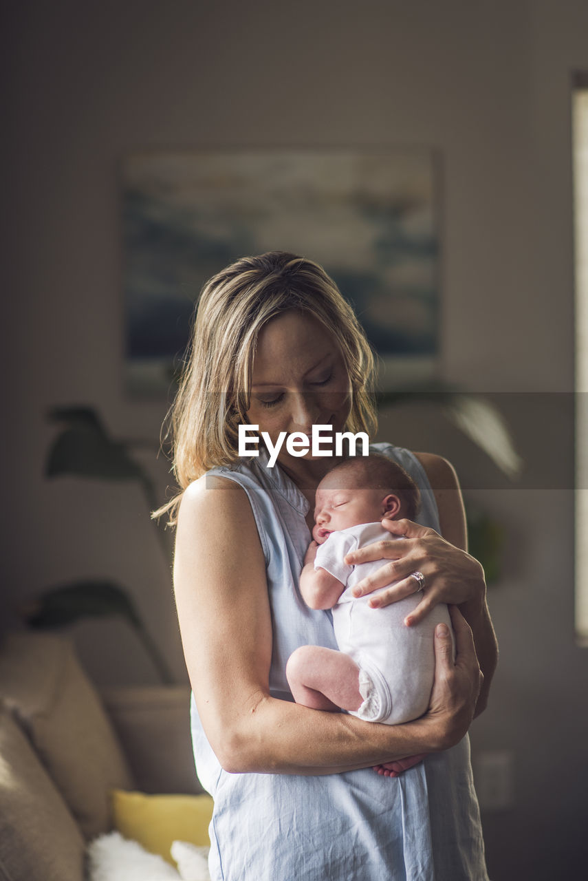 Smiling woman carrying son while standing in living room at home