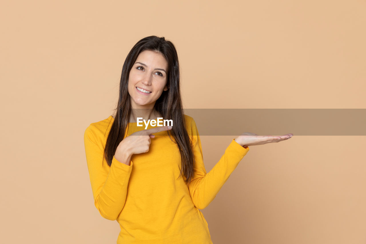 PORTRAIT OF A SMILING YOUNG WOMAN OVER YELLOW BACKGROUND