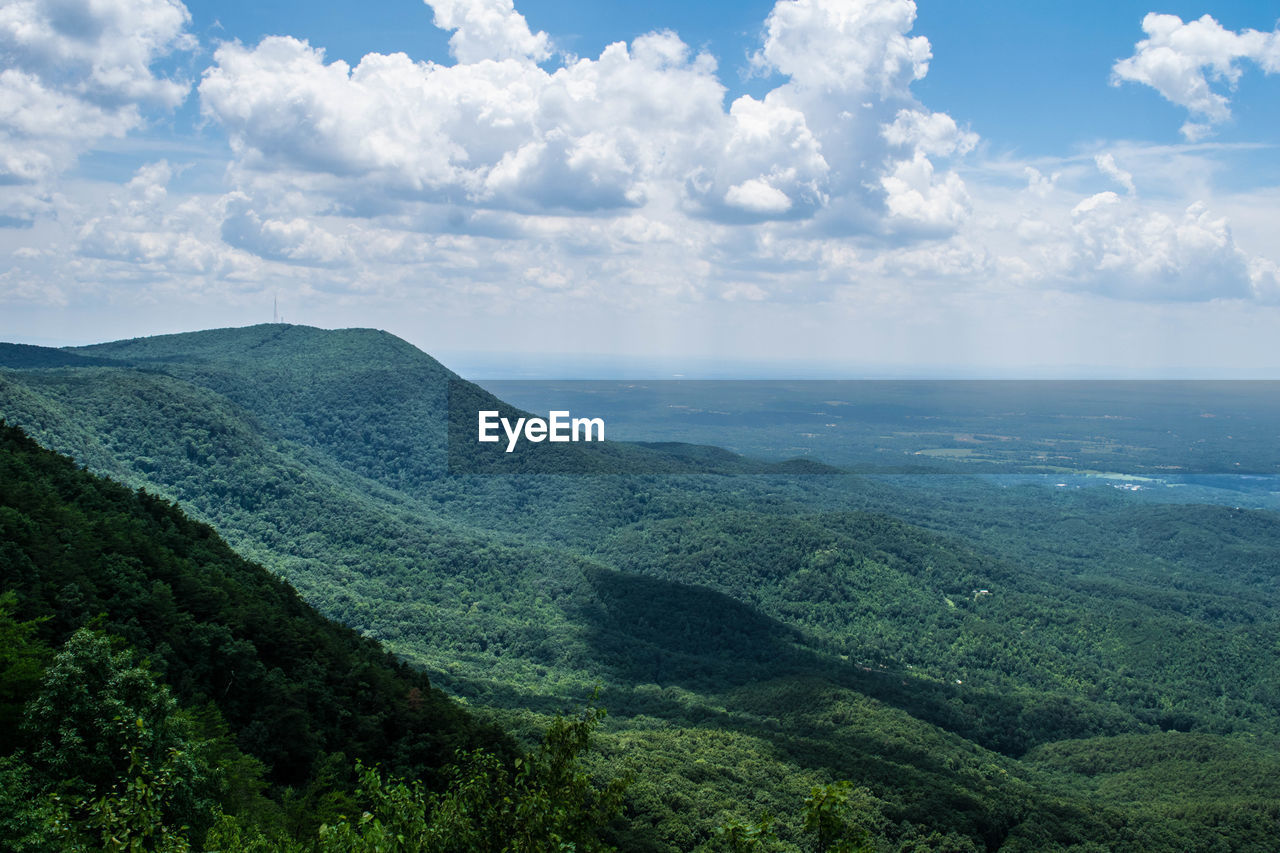 Scenic view of green mountains against cloudy sky during sunny day