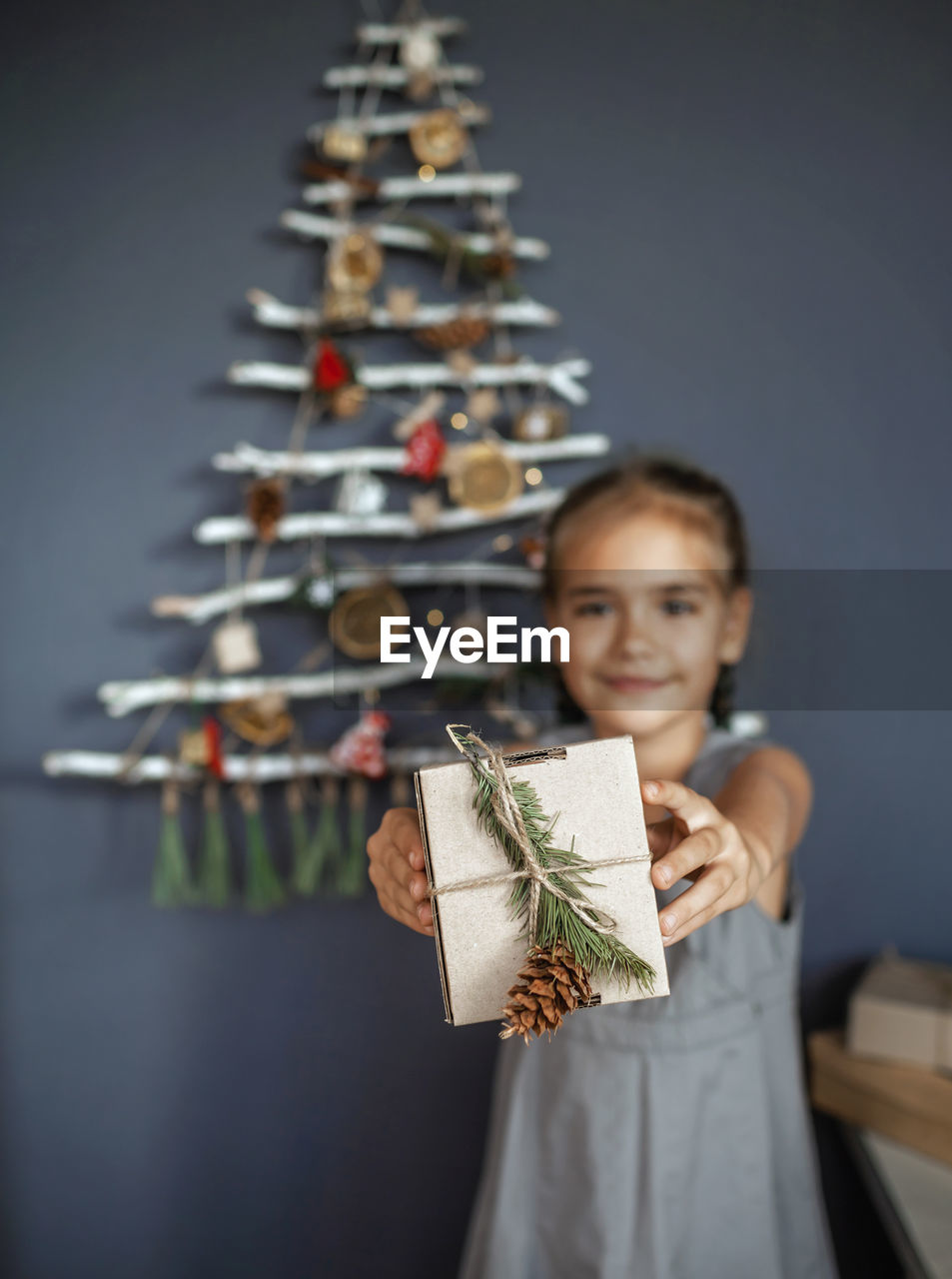 Happy girl holding present box near original christmas tree made with frozen branches, zero waste