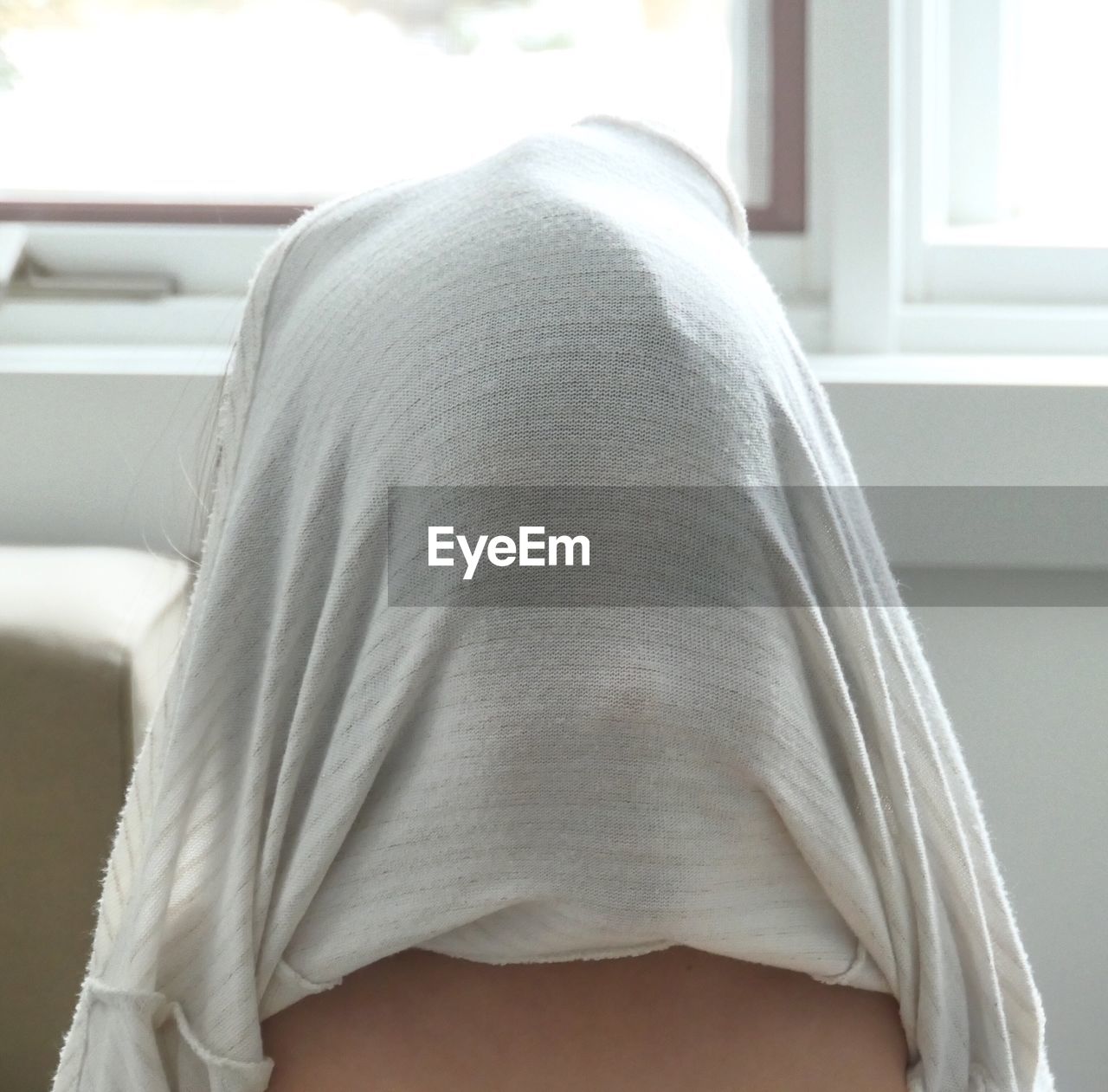 Person with t-shirt covering face at home