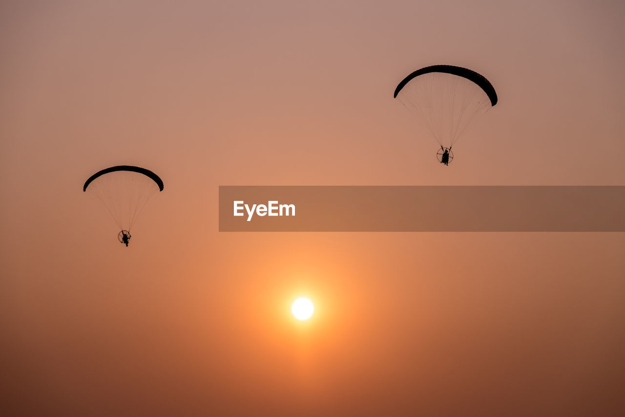 Low angle view of silhouette people paragliding against clear sky during sunset