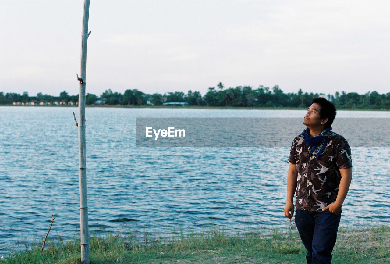 Man looking away while walking by lake against sky