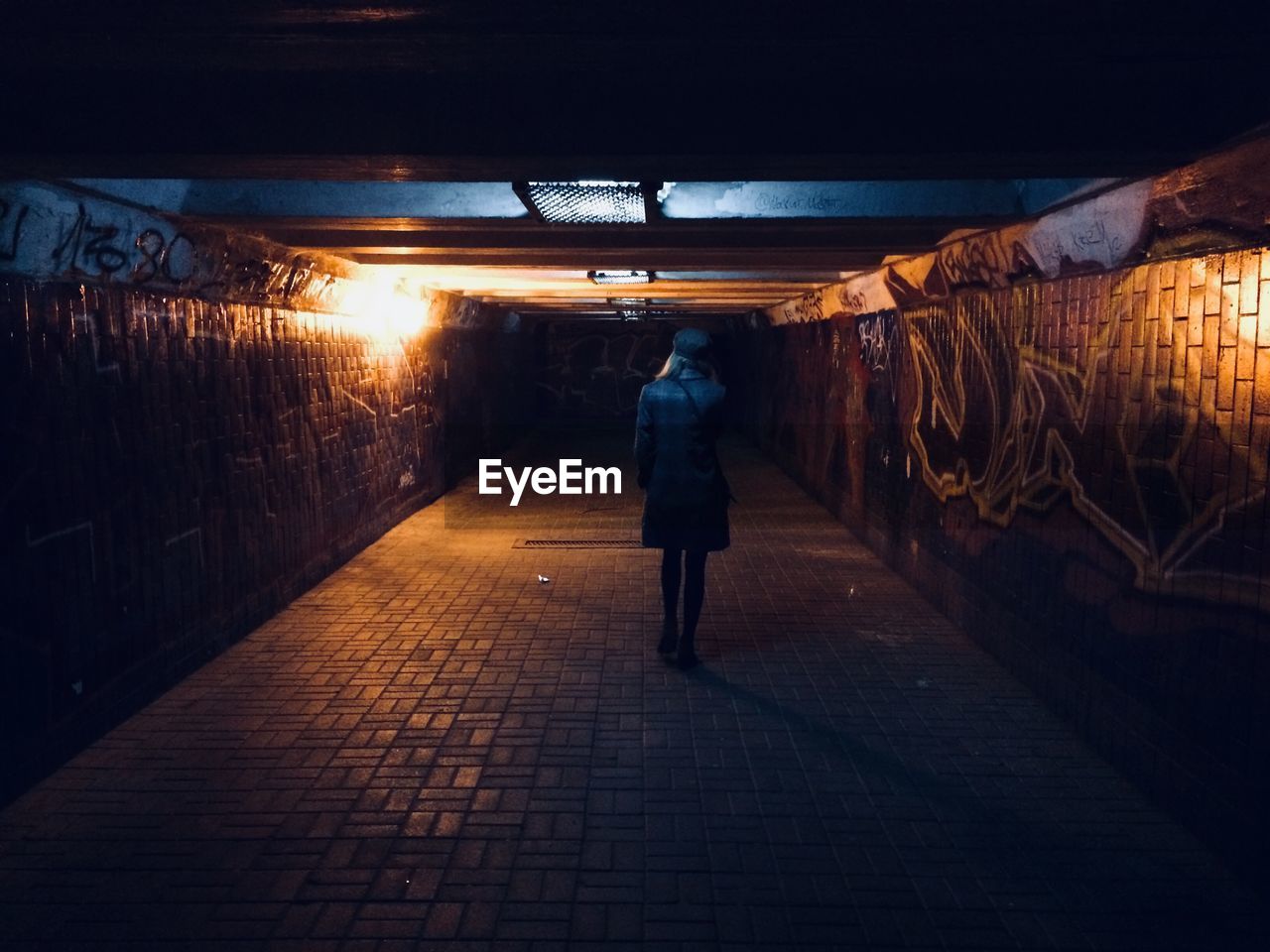 Rear view of woman walking on footpath in illuminated tunnel