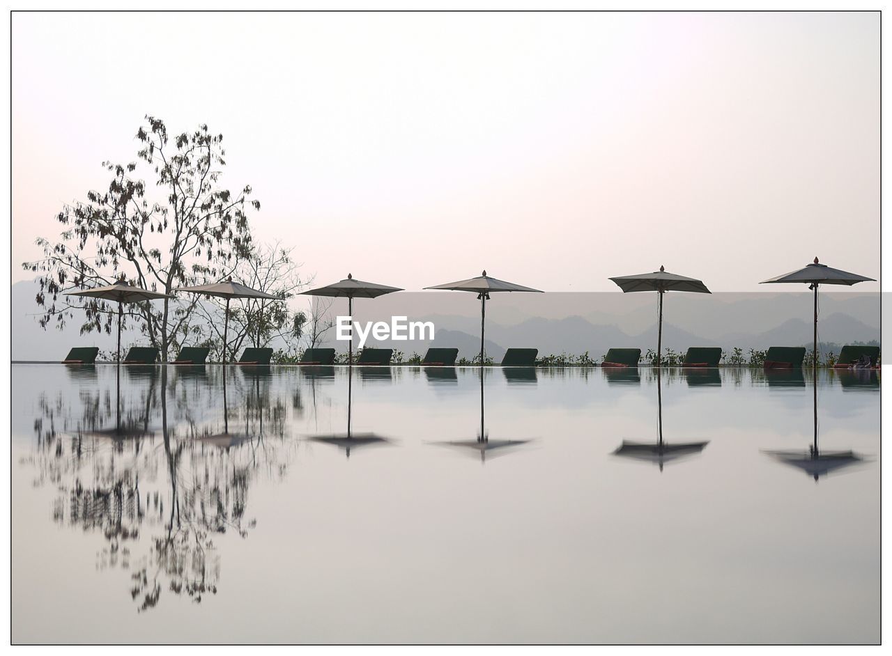Parasols reflecting in swimming pool against sky during foggy weather