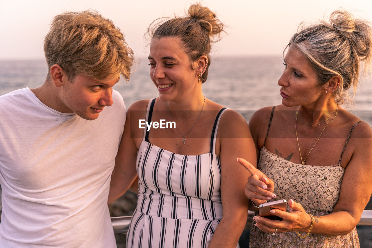 Beautiful mother with her twenty year old sons take a break by the sea at sunset - vacation concept