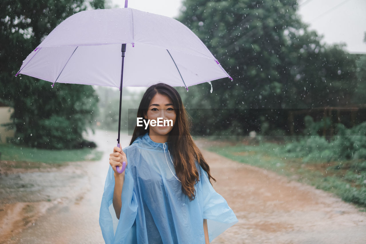 PORTRAIT OF SMILING WOMAN STANDING IN RAIN