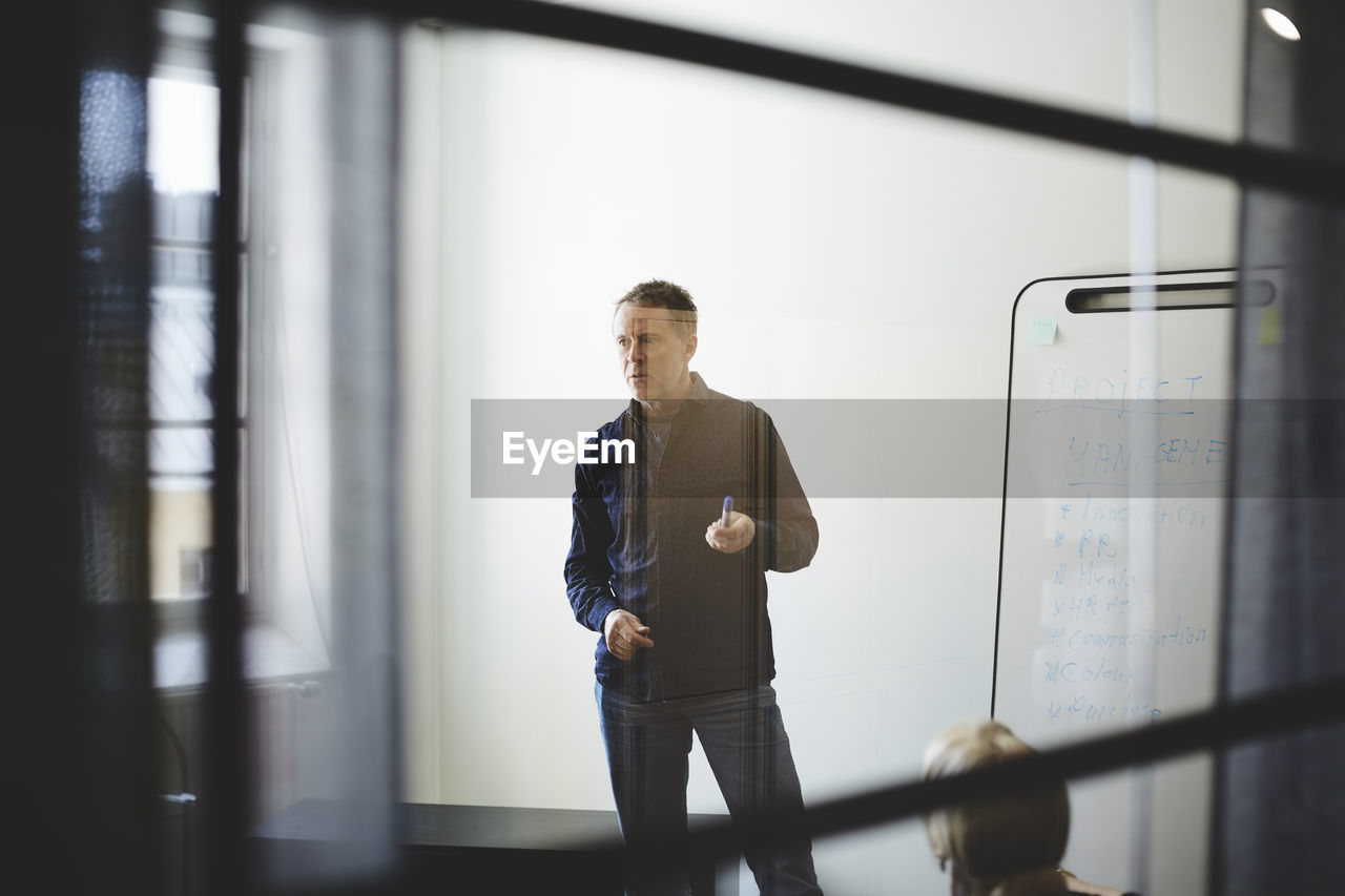 Businessman standing against white wall in board room seen from glass at creative office