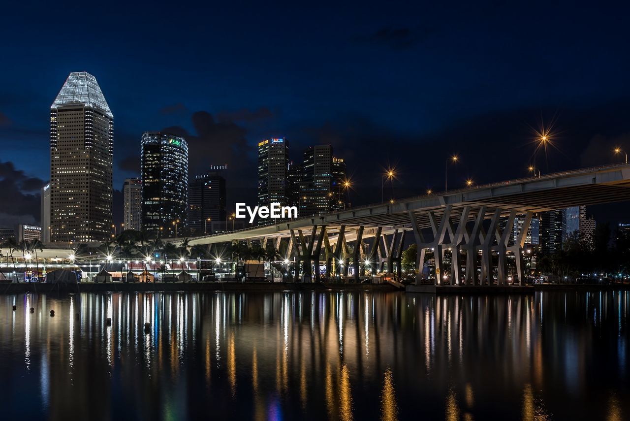 Illuminated buildings by river against sky at night