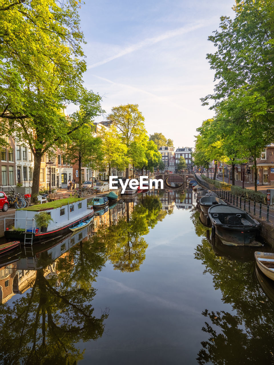 Serene amsterdam canal scene arched bridge, docked boats, and reflection in the still waters.