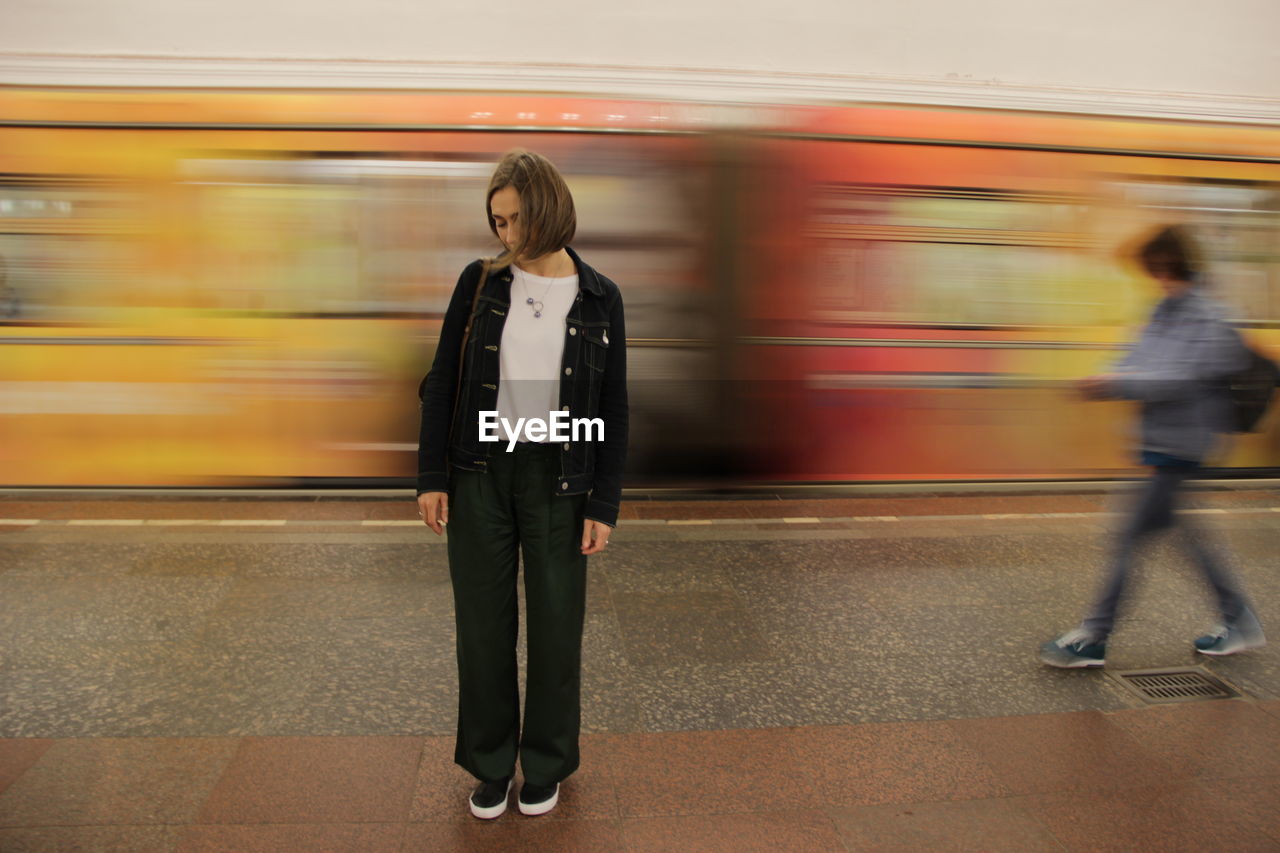 Blurred motion of train at railroad station and static girl